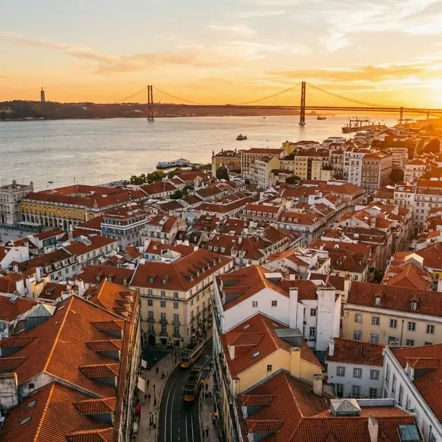 Vista panorâmica da cidade de Lisboa e do Rio Tejo ao pôr do sol, representando o destino de eleição para profissionais qualificados.